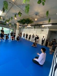 Eine Gruppe von Menschen sitzt auf einer blauen Matte in einem Fitnessstudio.